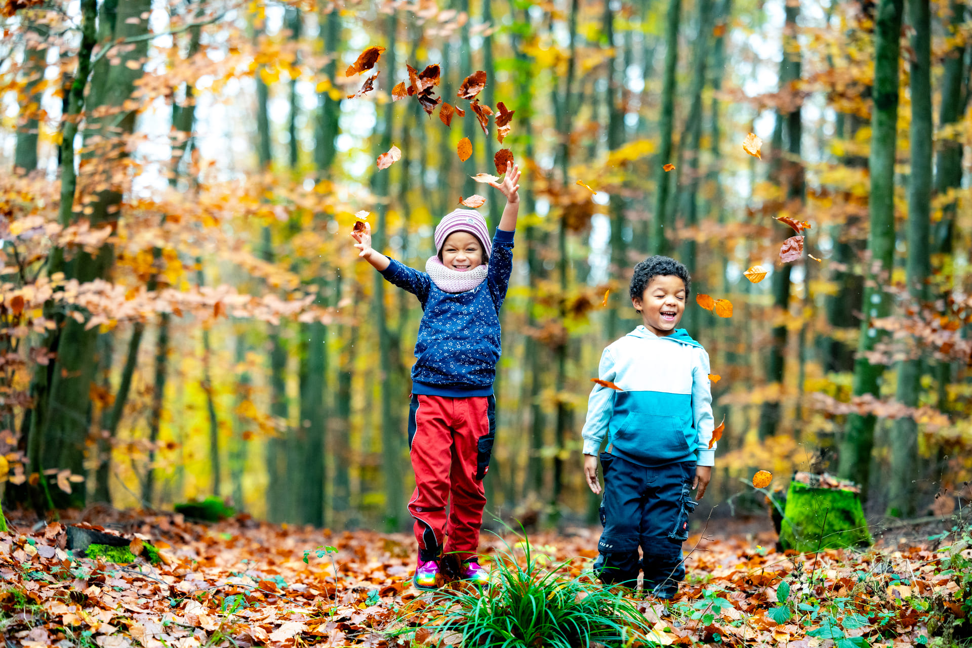 Zwei Kinder spielen im Herbstwald mit dem Laub