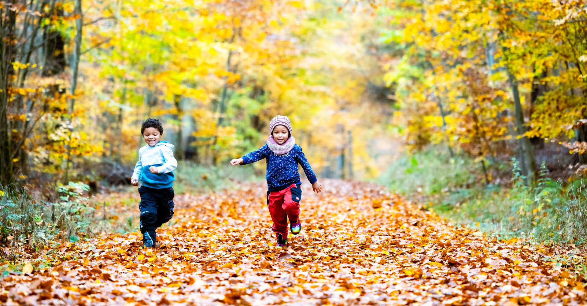 Zwei Kinder rennen im Herbstwald um die Wette